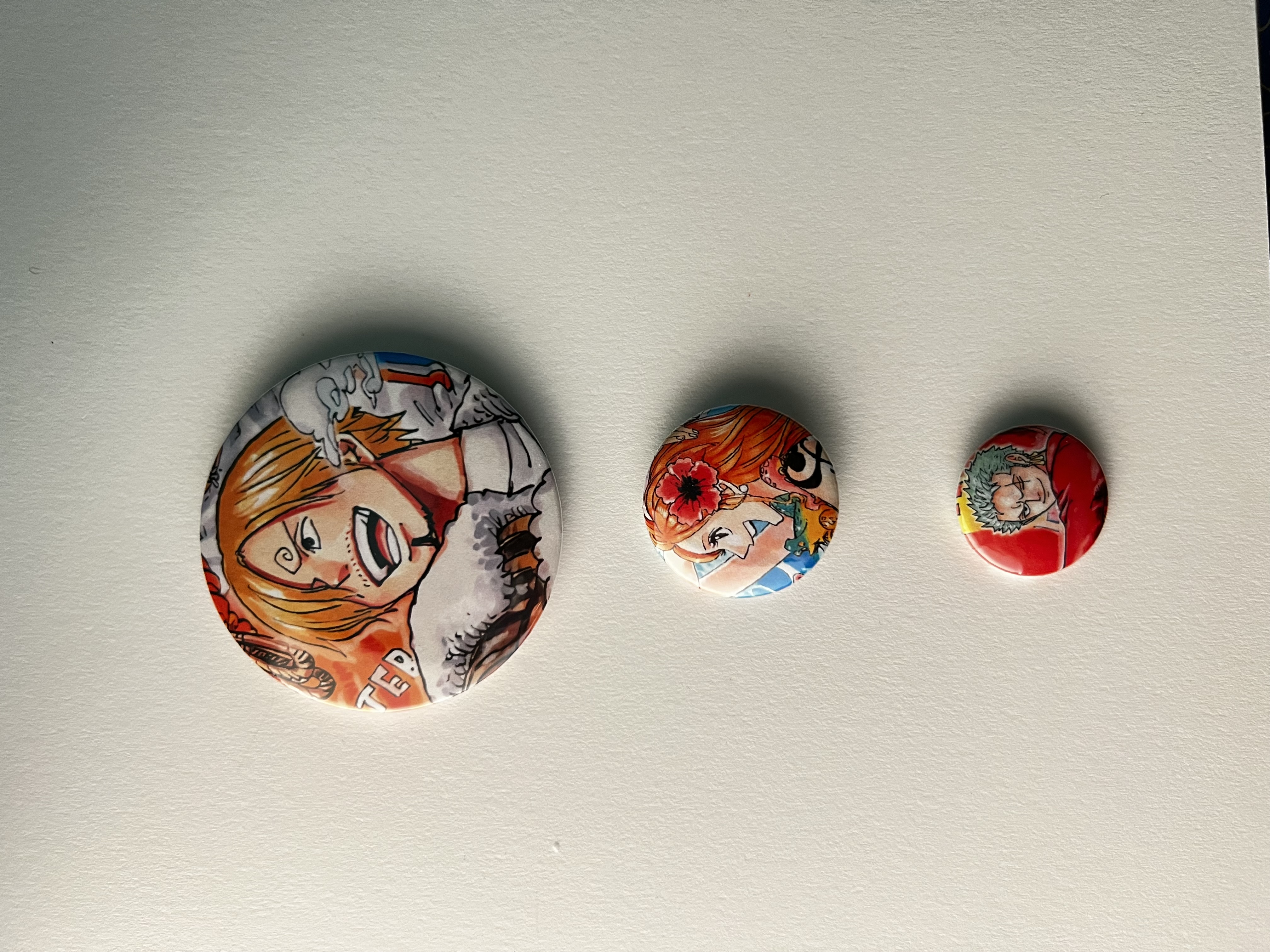 Handmade pin-back buttons shown in several sizes